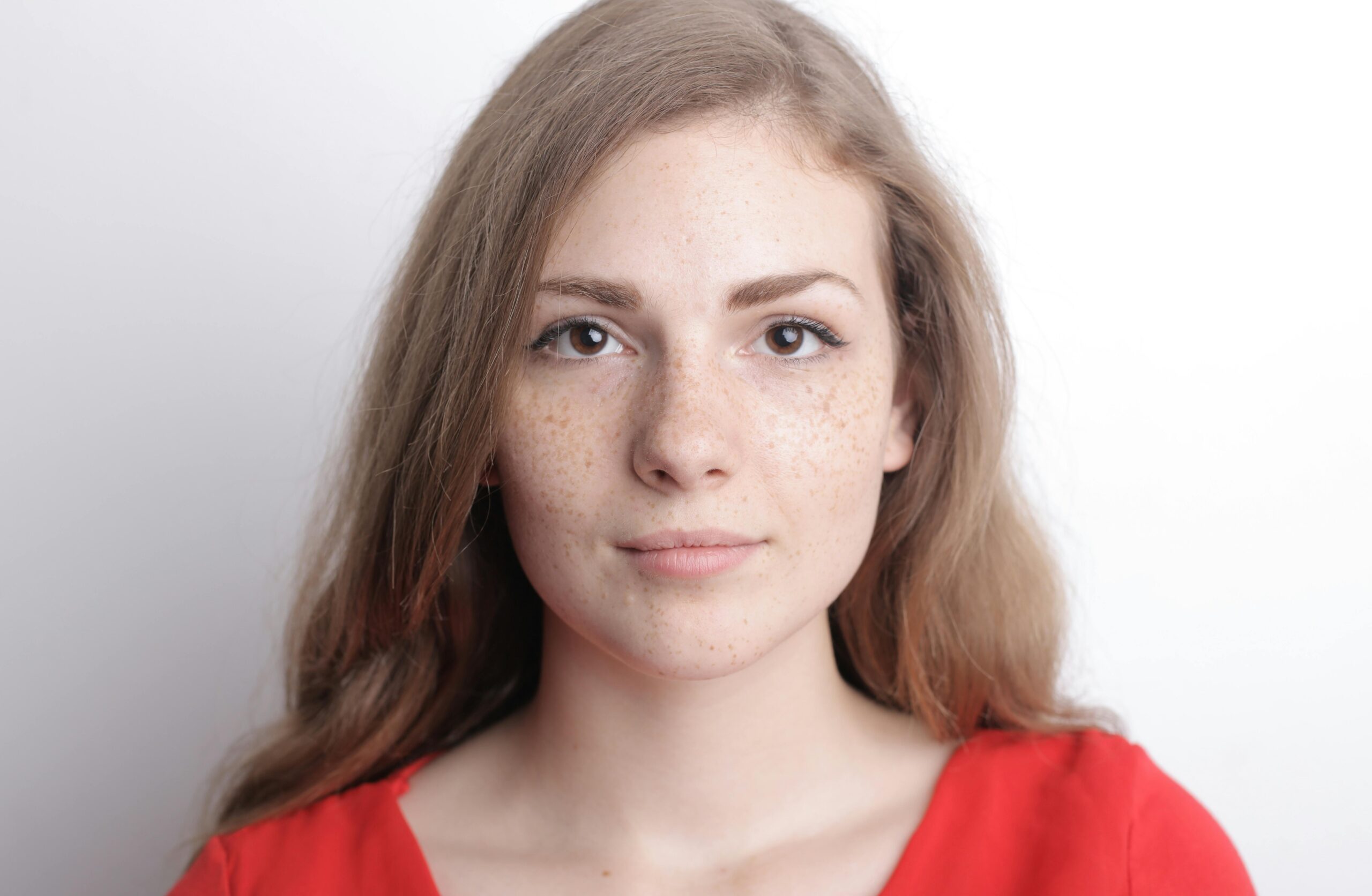 A close-up portrait of a young woman with freckles, long hair, and a calm demeanor.