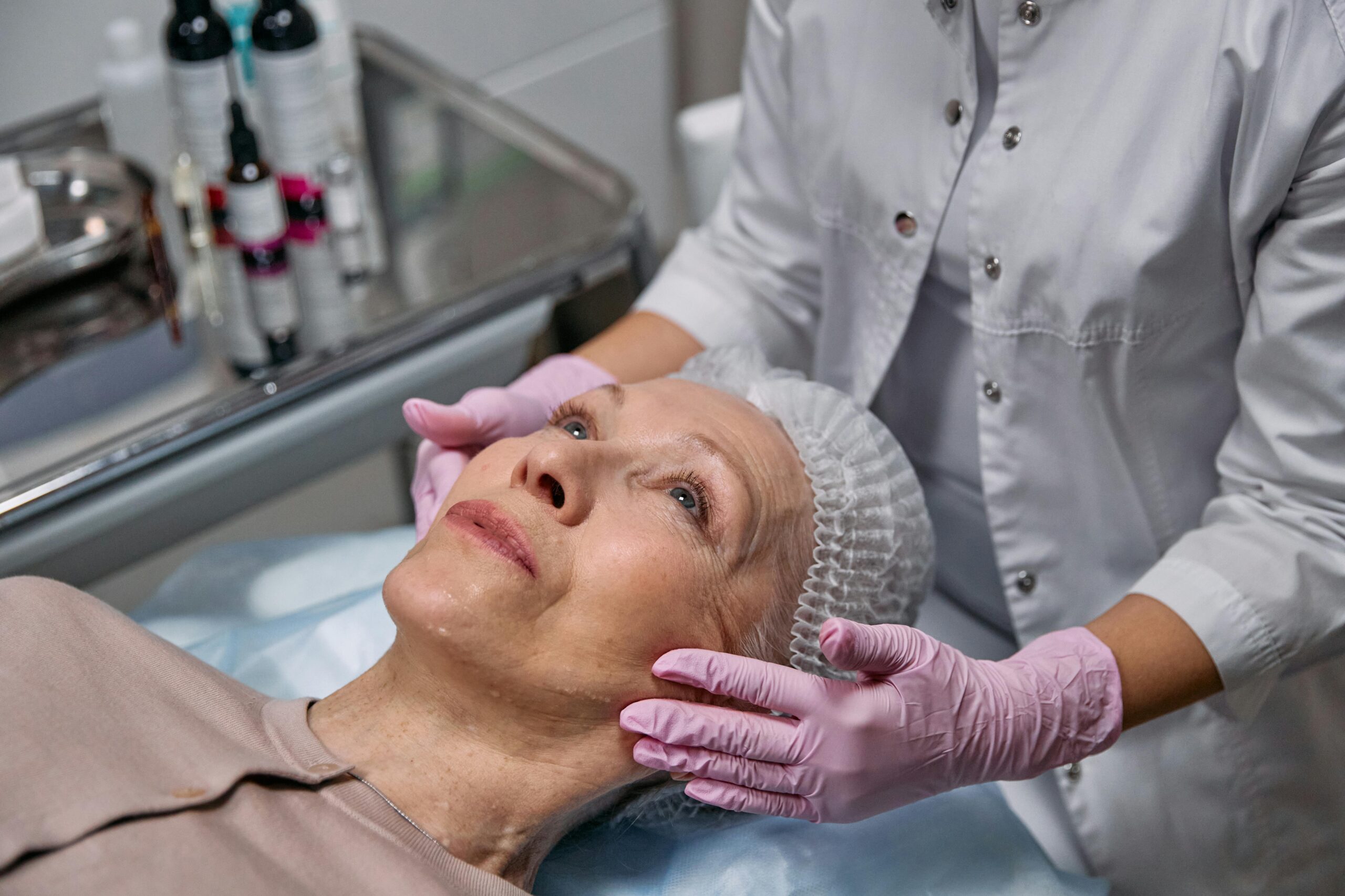 A mature woman in a spa receiving a relaxing facial treatment from a professional in a medical clinic setting.