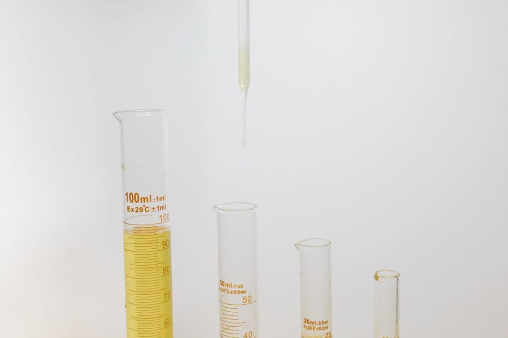 Close-up of laboratory glassware, including graduated cylinders and a pipette on a white background.