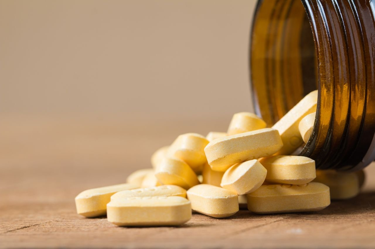 Folic Acid A close-up image of vitamin tablets spilling out of a transparent brown bottle on a wooden surface.