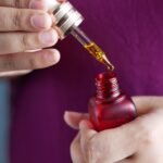Detailed image of hands using a dropper with a red glass bottle. Perfect for skincare and beauty themes.