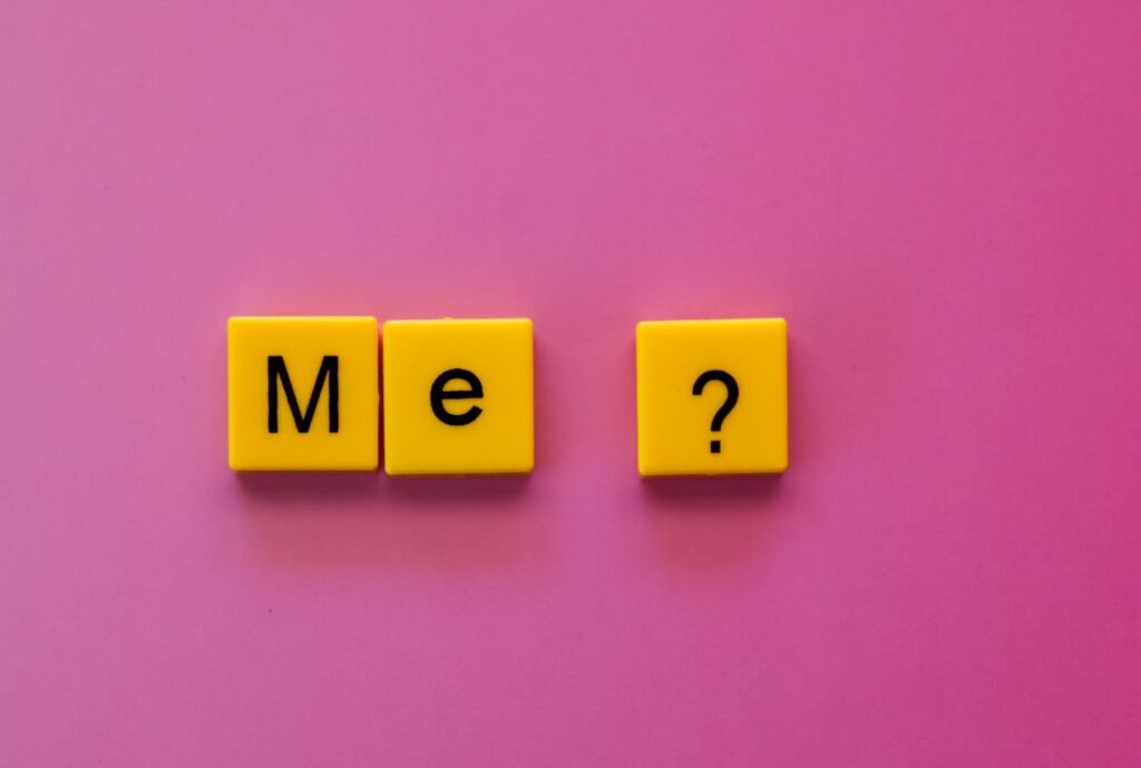 Yellow letter tiles forming 'Me?' against a vibrant pink background, offering a playful concept.
