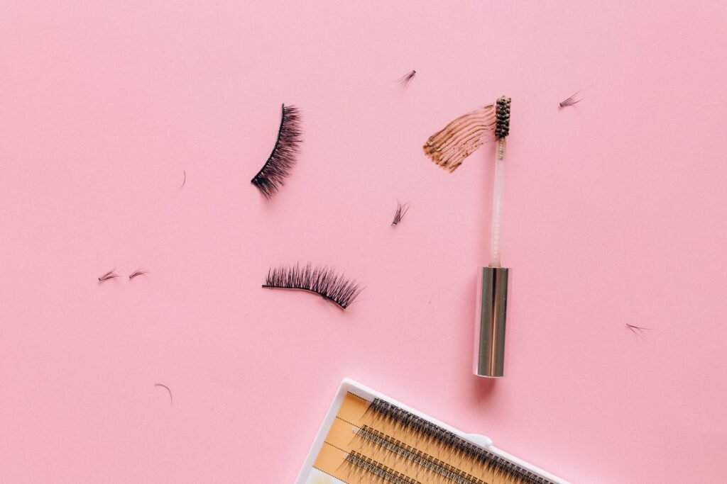 Styled flat lay of false eyelashes and makeup brush on a pastel pink surface.